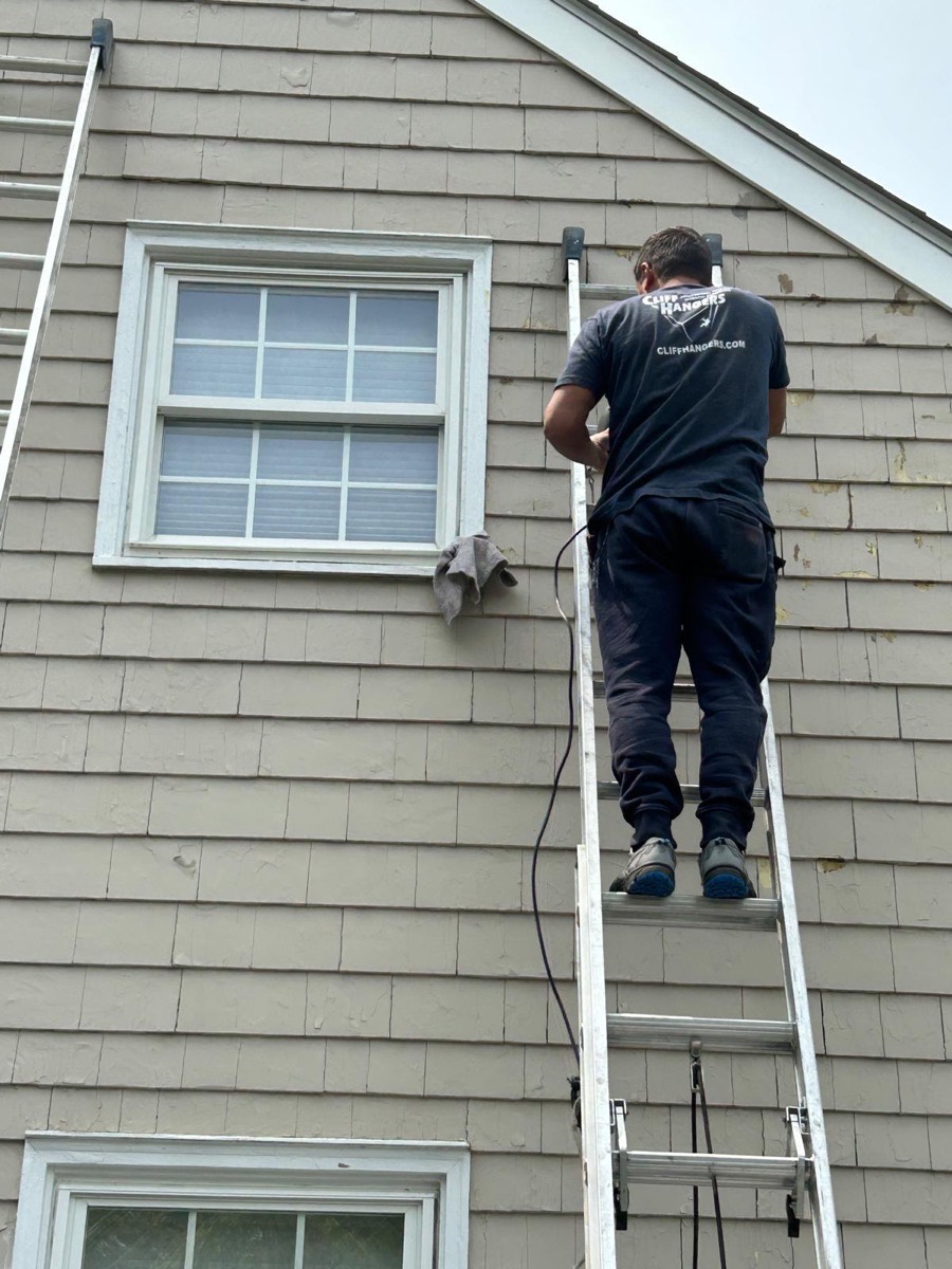 Painter on a ladder preparing cedar shingle siding