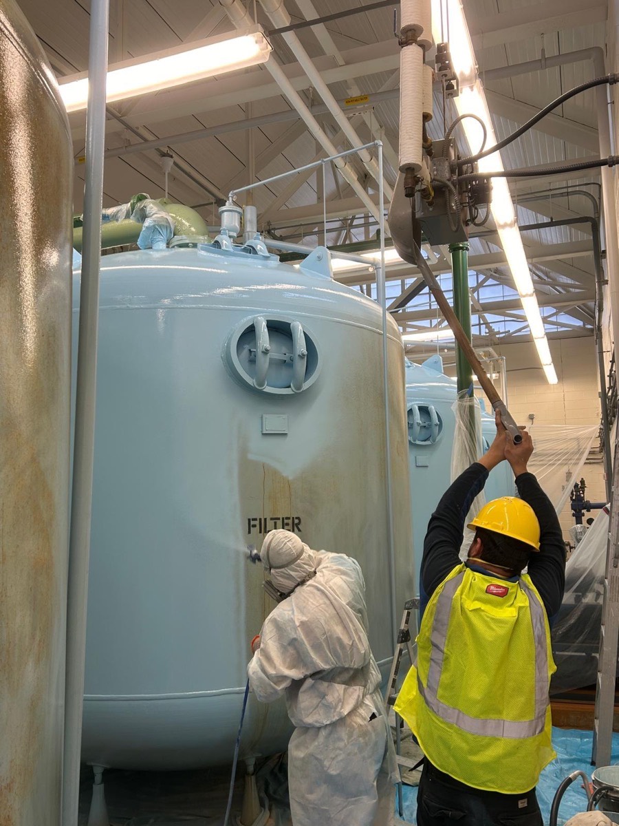 Painters in protective suits coating large industrial tanks