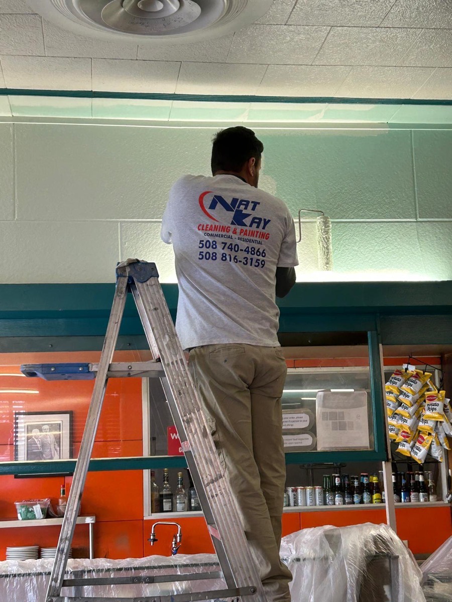 Kay painting the walls of a store interior from a ladder