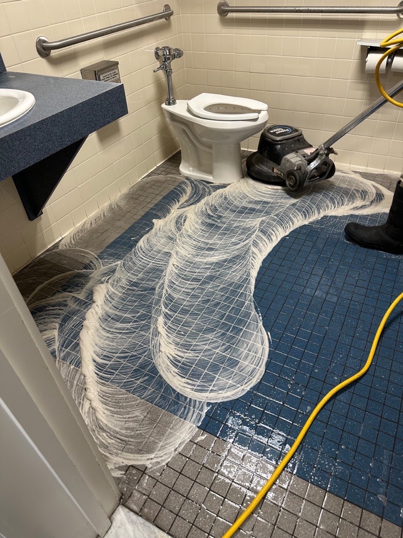 Commercial restroom tile floor being machine-scrubbed with foam