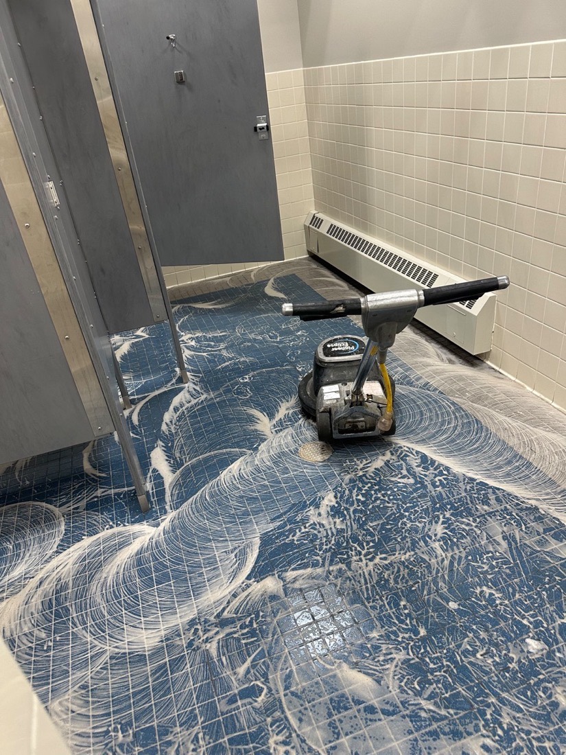 Floor scrubbing machine cleaning a blue tile restroom floor